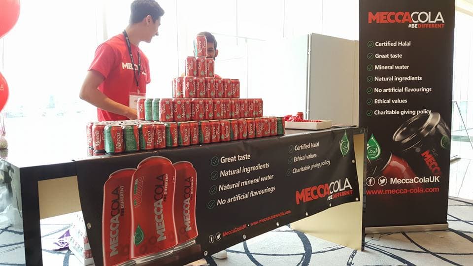 Stand Mecca Cola au Royaume-Uni : pyramide de canettes et kakémono « Certified Halal »
